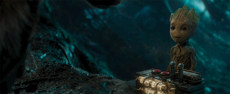 A gif of baby Groot from Guardians of the Galaxy Vol.2. He is in a cave-like atmosphere and stands in front of a control box with two red buttons and two large levels. He looks up at Rocket, who is offscreen, and then looks down at the control box and points at one of the red buttons. Rocket’s hands appear on-screen, motioning that he is pointing towards the wrong red button.