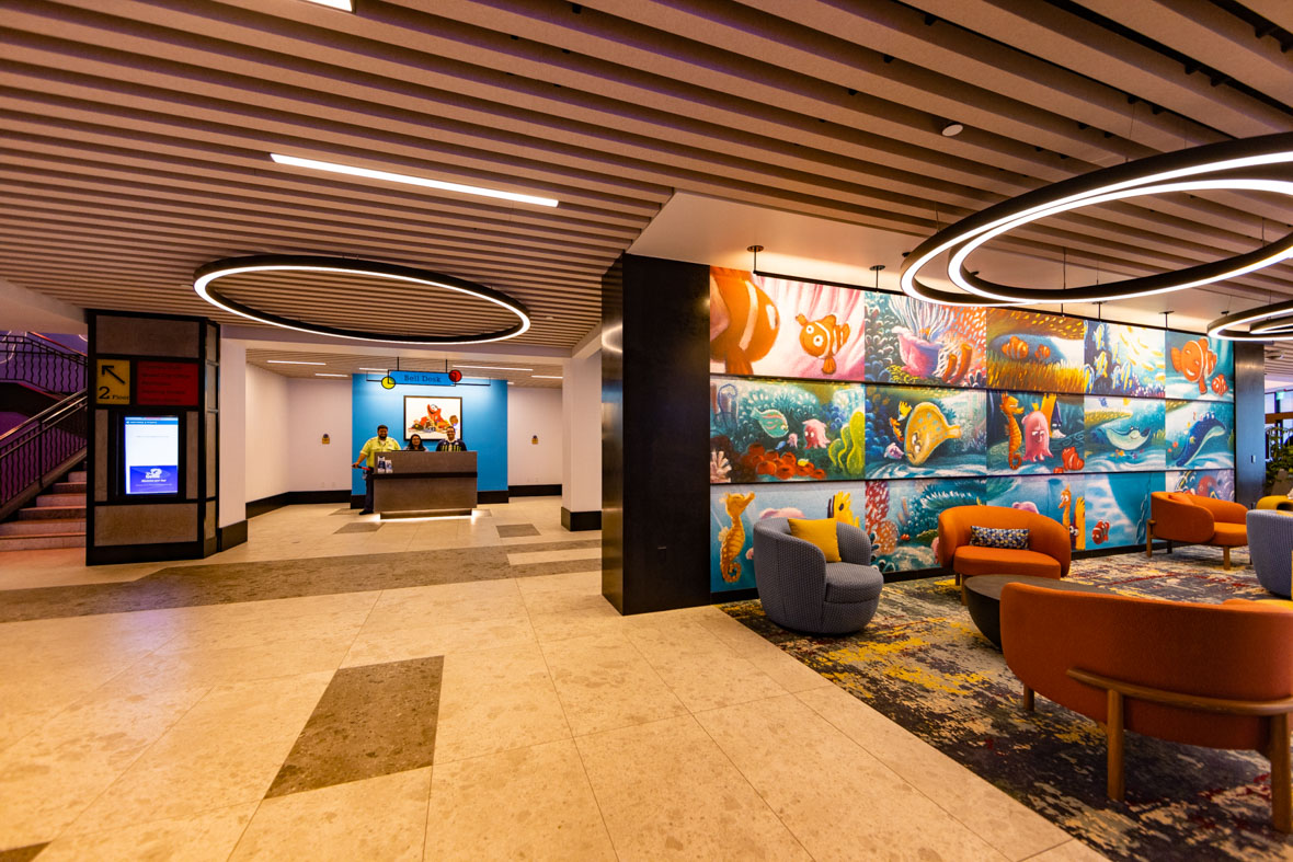 The lobby of Pixar Place Hotel feature colorful upholstered furniture and a wall mural of images from Pixar Animation Studios’ Finding Nemo.