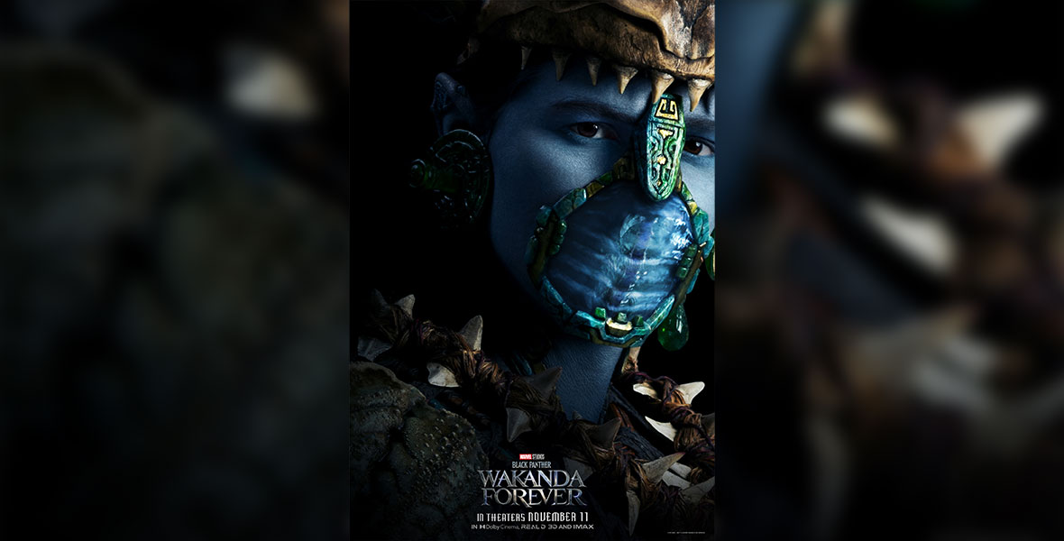 A portrait of Attuma (Alex Livinalli), a blue-skinned man wearing a headdress, spiky shoulder pads, and a breathing mask. He is emerging from the darkness and staring head-on at the camera.