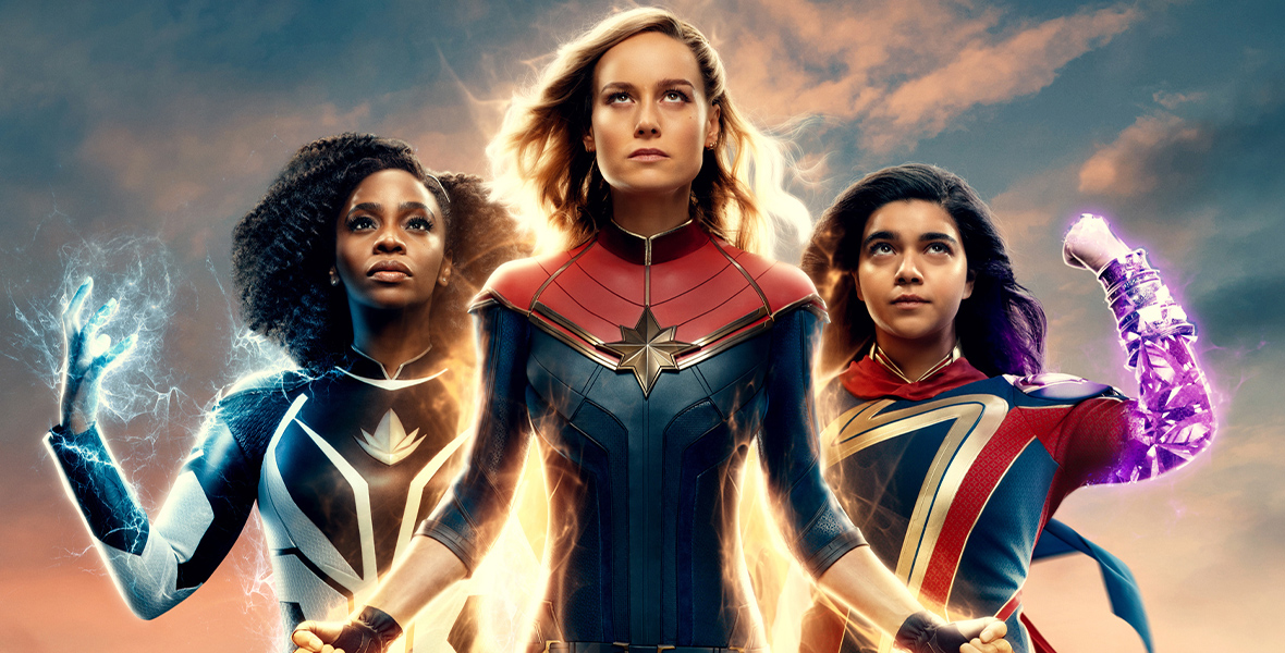 In a promotional poster for Marvel Studios' The Marvels, Monica Rambeau, played by Teyonah Parris, Carol Danvers, played by Brie Larson, and Kamala Khan, played by Iman Vellani, strike classic Super Hero poses. They respectively emit white, gold, and purple light.