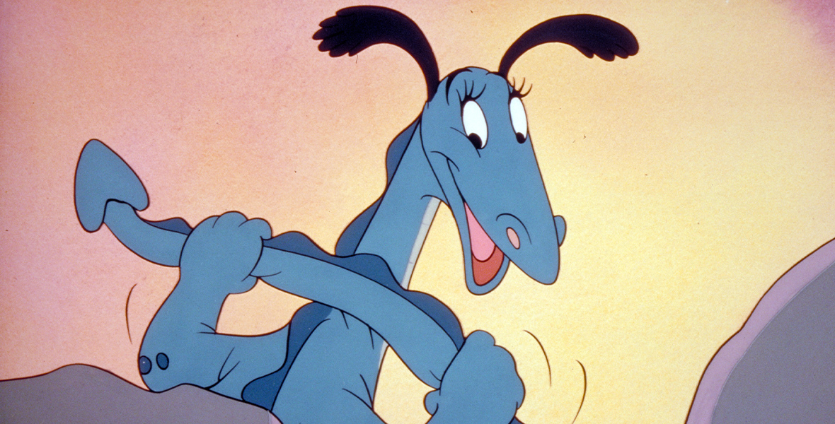The Reluctant Dragon is large and blue with black ears. Its back is facing the camera, with its head turned toward the camera, smiling, and holding its tail.