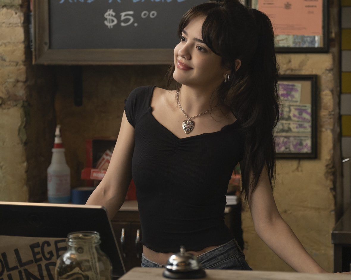 In an image from Goosebumps: The Vanishing, Frankie Garcia Bravo (Galilea La Salvia) stands behind the counter at a shop, with a cash register and bell on the counter in front of her. She is looking off to the left with a sarcastic expression, leaning away from what she’s looking at offscreen.