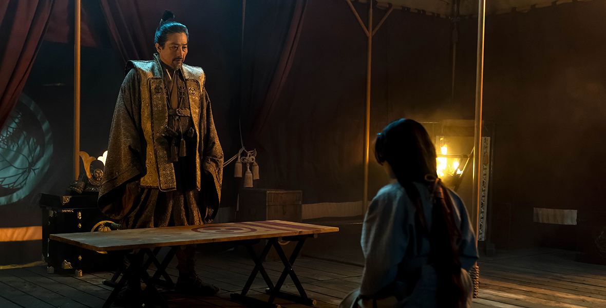 In a scene from the television show Shōgun, Hiroyuki Sanada (Lord Yoshi Toranaga) is standing and wearing a gold kosode. Anna Sawai (Toda Mariko) kneels in front of Yoshi Toranaga and is wearing a light blue kosode. Courtesy of FX Networks. 