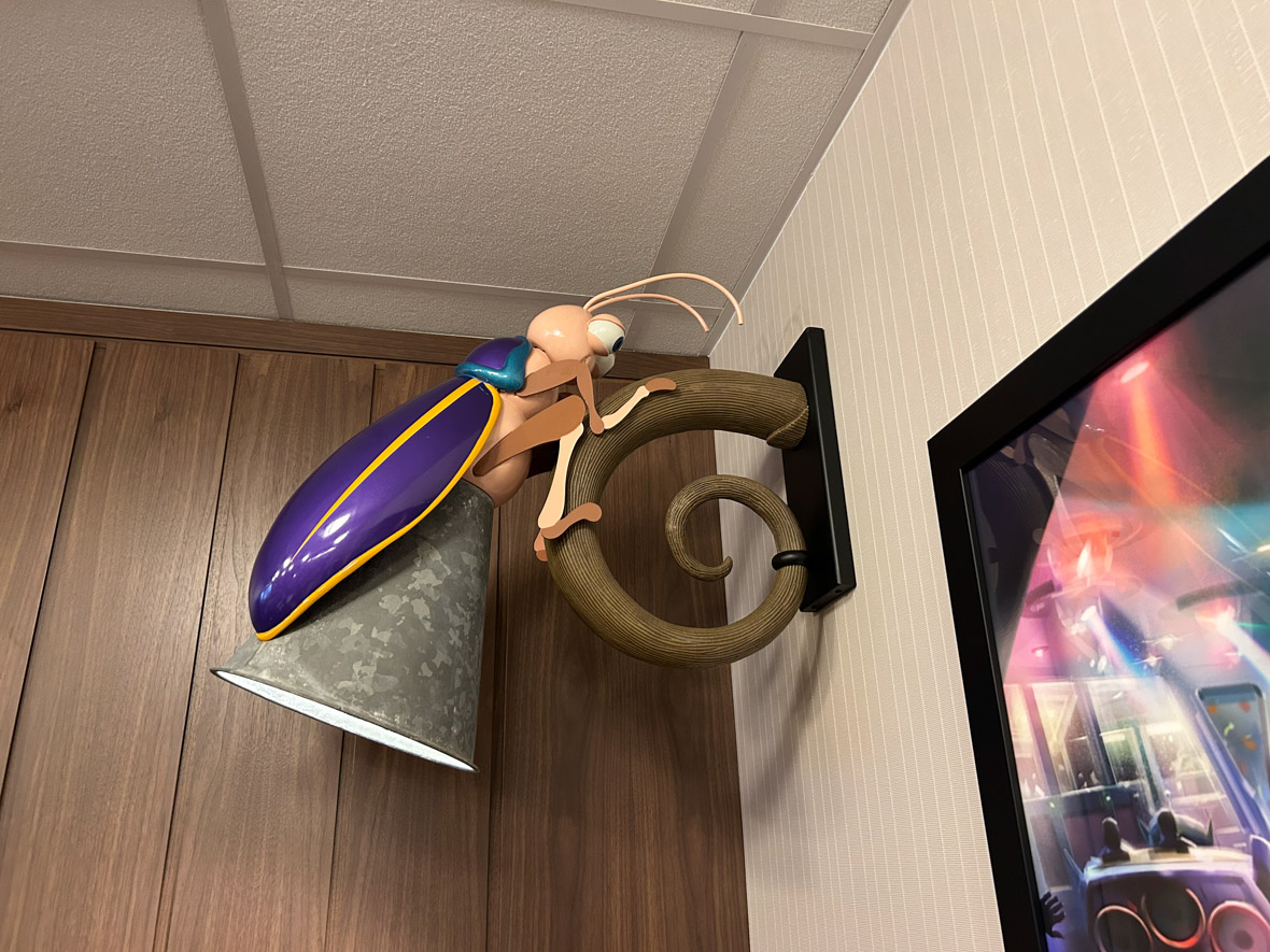 A wall sconce designed to look like a firefly is shining its light down into the room. The firefly is stylized to look like a bug from Pixar’s A Bug’s Life.